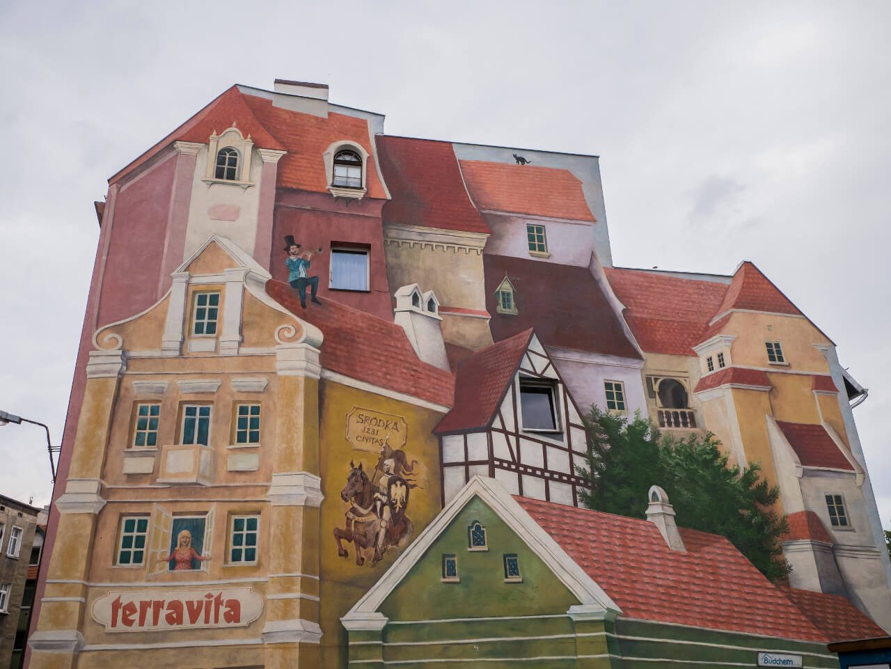 Zbliżenie na mural "Opowieść śródecka z trębaczem na dachu i kotem w tle"